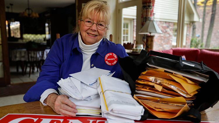 In this Thursday, Oct. 31, 2019, photo, Sue Dillon poses in her home in Carmel, Ind., with some of the petitions gathered to change Indiana time zone. Dillon became a campaigner for changes to the state's time choice after a teenager was fatally struck in 2009 while running to catch a school bus in the early morning darkness near her home.  - AP Photo/Michael Conroy