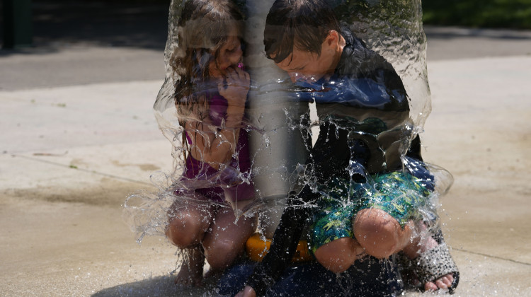 Miles Ruffing and his sister, Frances, play under a water sprinkler while playing at Broad Ripple Park, Friday, June 21, 2024, in Indianapolis. - Darron Cummings / AP Photo
