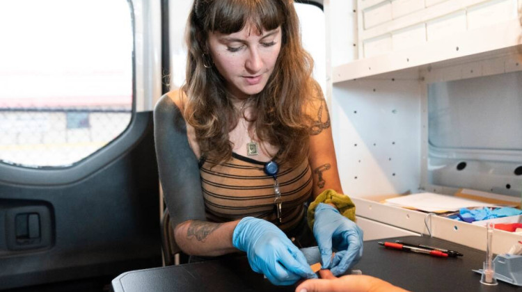 Hana Fields, outreach manager for HOPE in Tulsa, Okla., bandages a patient's finger after taking a blood sample. - Nick Oxford / Tradeoffs